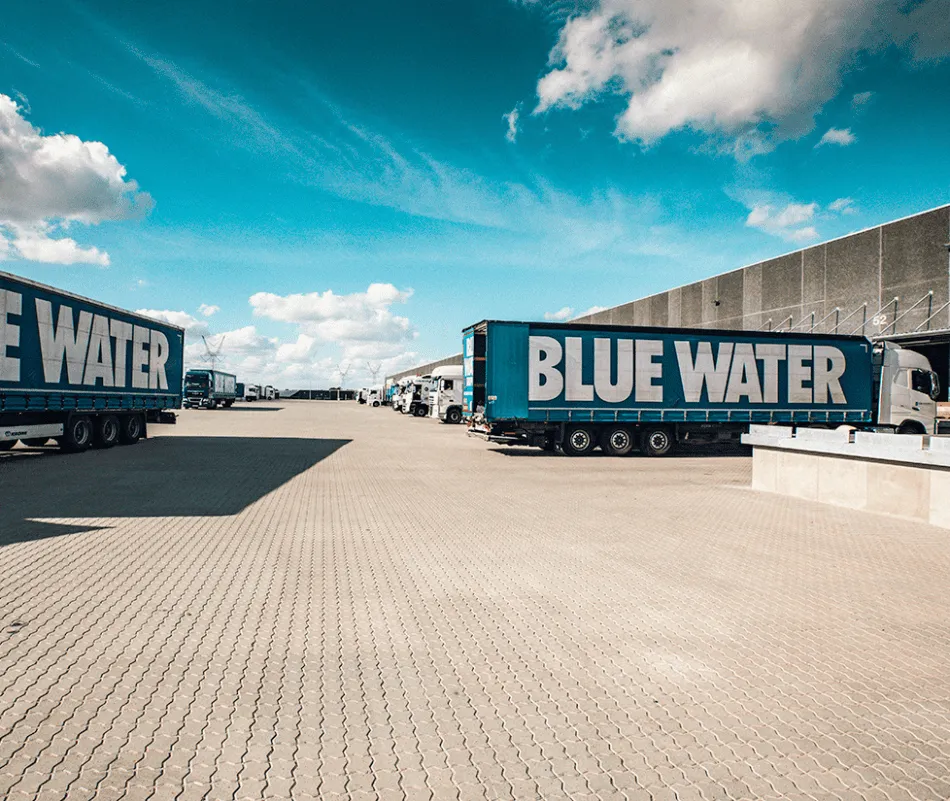 Blue Water trucks outside a warehouse under a blue sky.
