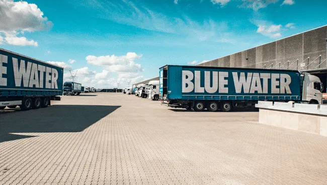 Blue Water trucks outside a warehouse under a blue sky.